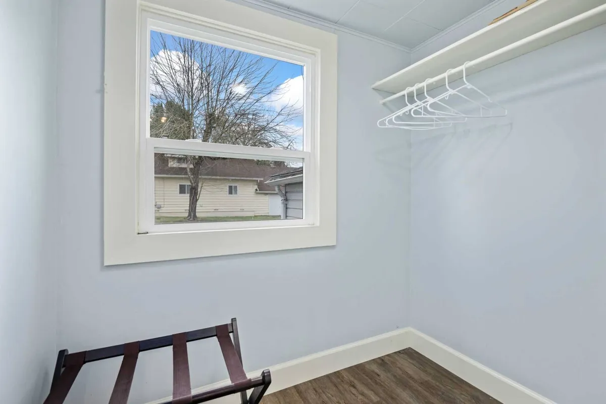 This image shows a tranquil corner of the home featuring a window with a view, a wooden folding stool, and a shelving unit. The natural light streaming in and the peaceful setting evoke a sense of restful retreat and relaxation.