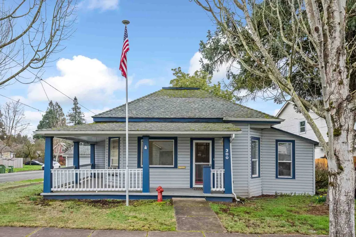 The image features the inviting front porch of a charming bungalow, set on a corner lot with a classic flag pole and a cheerful red fire hydrant nearby. The scene exudes small-town warmth, perfect for relaxing evenings and friendly gatherings, with the porch positioned to catch beautiful sunsets.