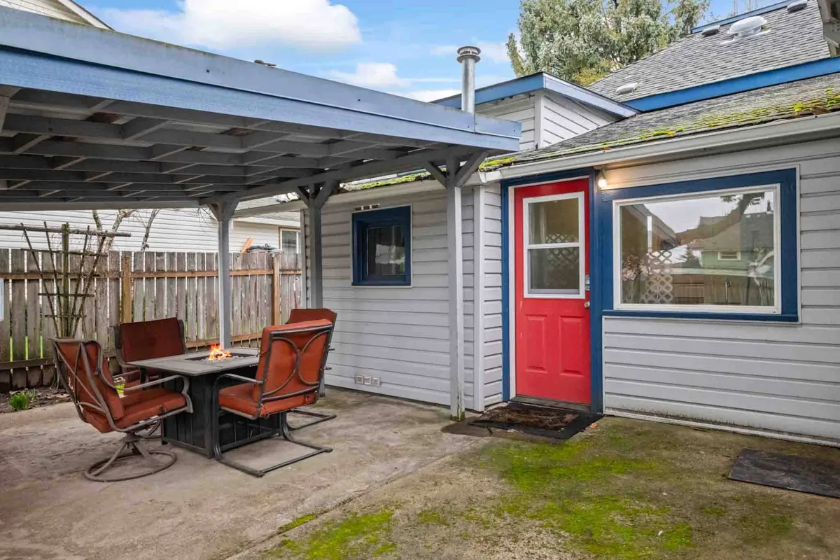 A cozy view of a patio area with seating under a covered structure, featuring a red door and an inviting atmosphere for morning coffee or evening gatherings. The covered area ensures comfort regardless of the weather and visually extends the living space outdoors.