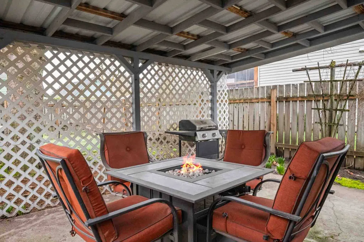 An inviting exterior setup showcasing an intimate fire pit with cushioned outdoor seating and a grill nearby. The setting is designed for evening relaxation, shared stories, and meals cooked outdoors, emphasizing the warmth and camaraderie of Pacific Northwest evenings.